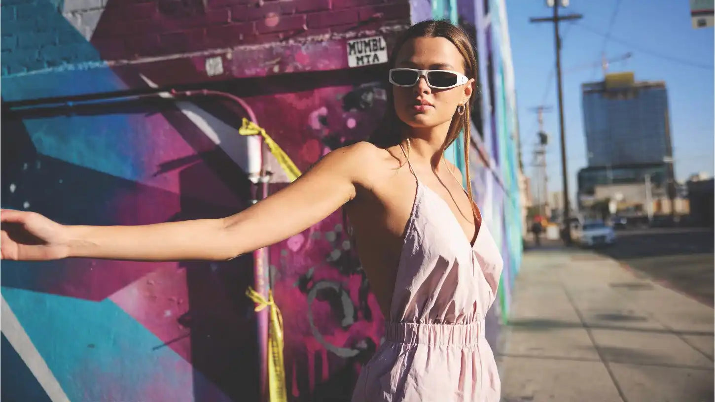 Woman in a light pink romper and white sunglasses.